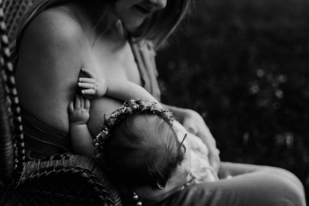 Intimate black and white photo of parent holding baby with floral crown outdoors.