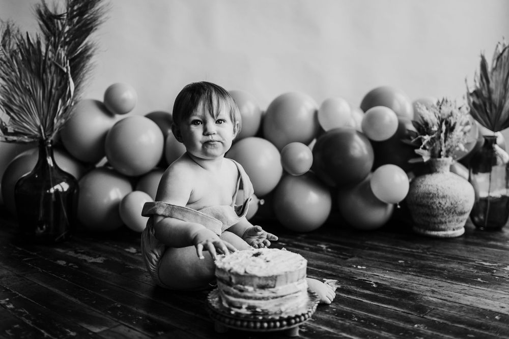 A first birthday celebration with balloons and cake on a wooden floor.