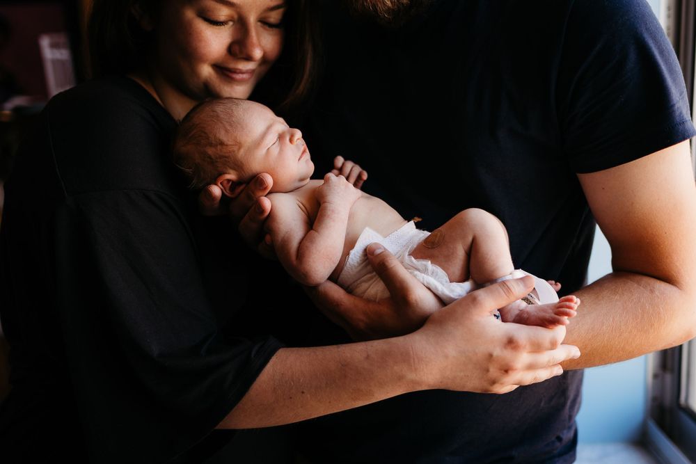 Tender moment of parents holding newborn baby in natural window light.
