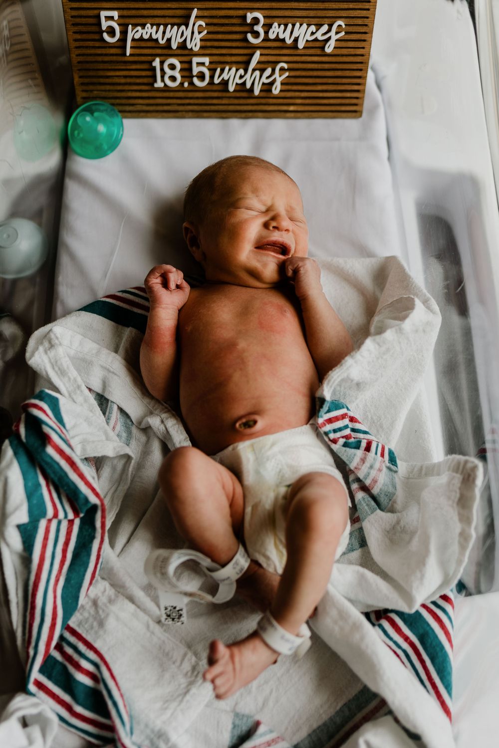 A newborn baby lying on a striped blanket with a wooden sign showing measurements above.