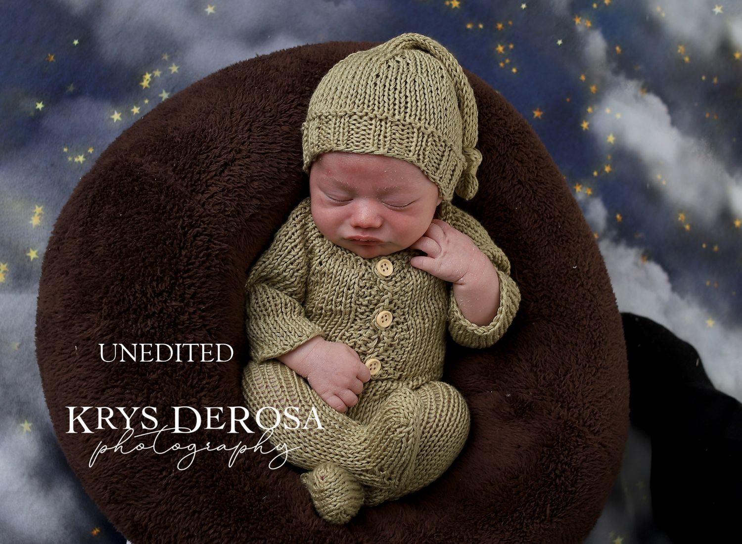 Newborn in green knit outfit sleeping on dark brown backdrop with starry effect.
