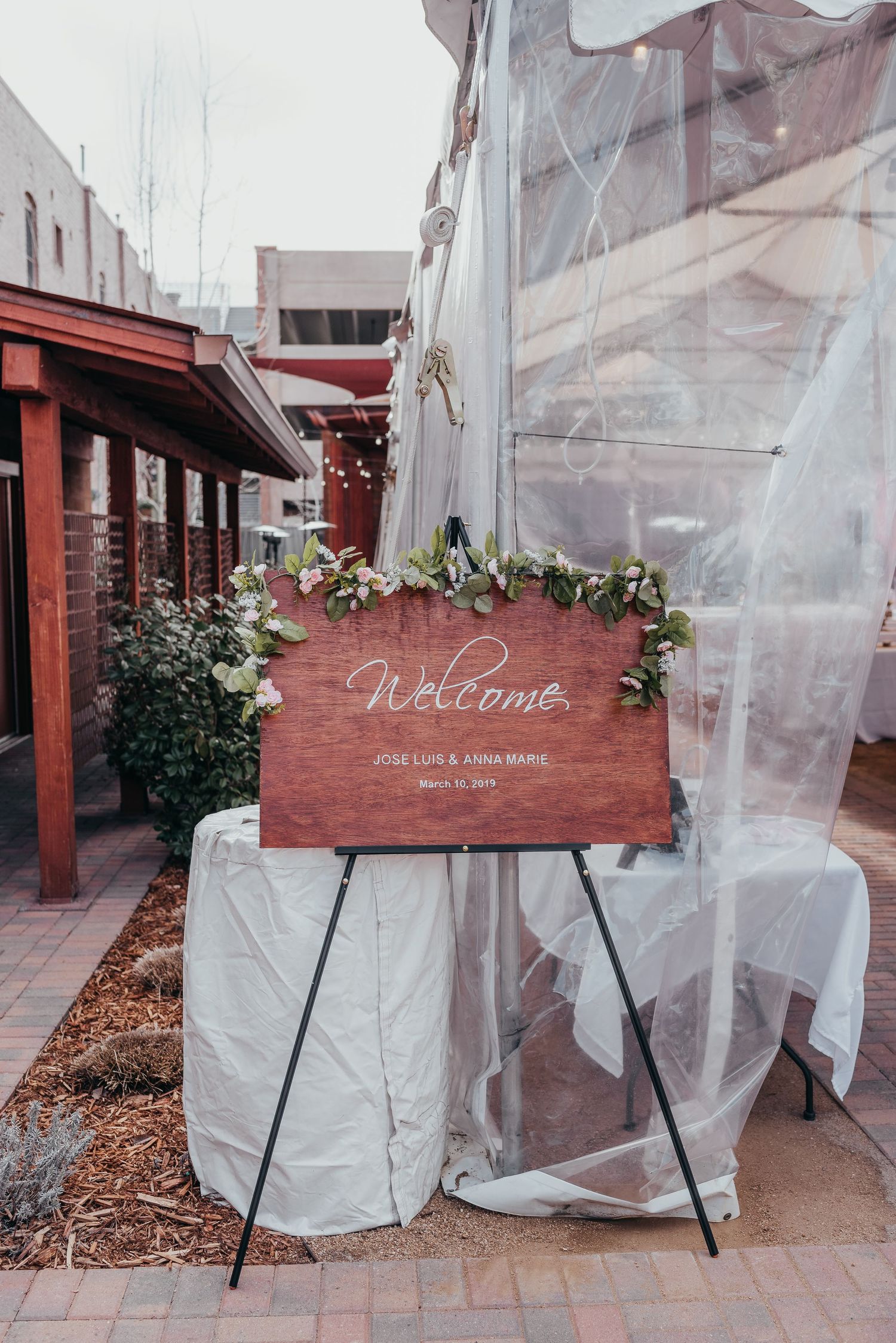 Rustic wooden welcome sign displayed at outdoor wedding venue with white tent backdrop.