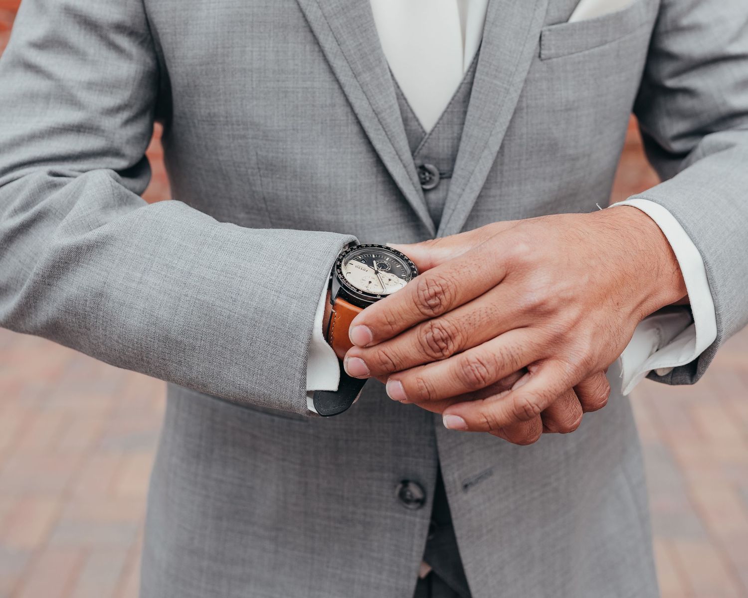 Close-up of a groom's hands adjusting his watch while wearing a grey three-piece suit.
