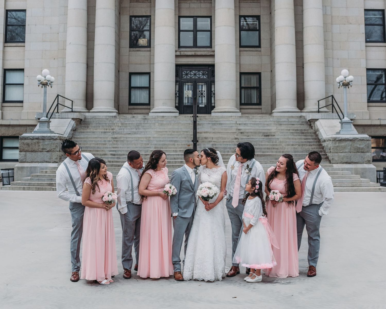 Wedding party in pink and grey attire posed on steps of historic building.