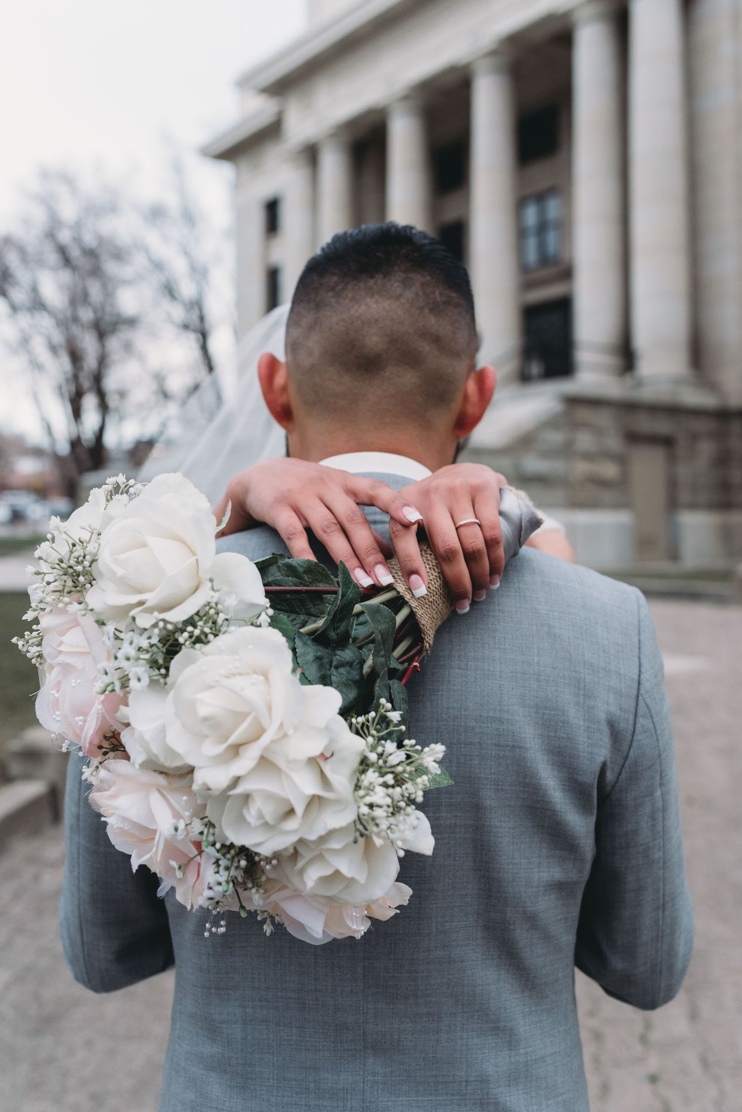 Close-up of white rose bouquet against grey suit at formal event.