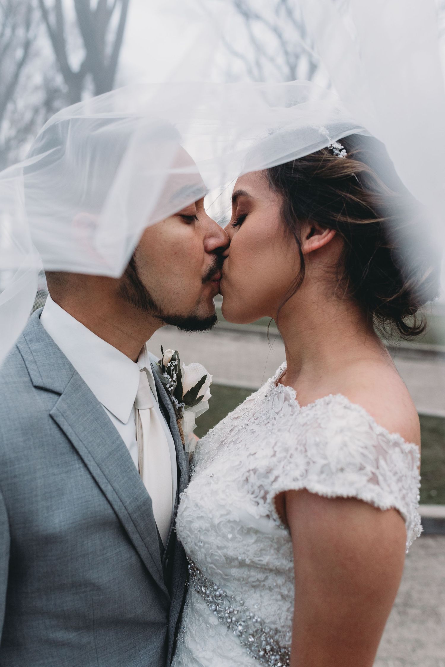 A couple shares their first kiss as newlyweds, with the bride in lace and groom in grey suit.