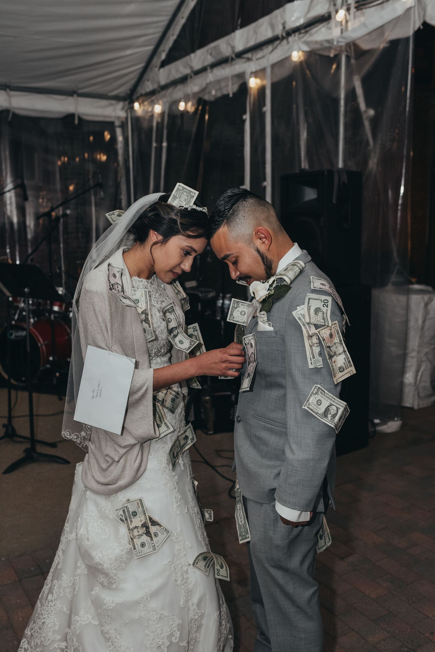 Couple in wedding attire performing money dance with dollar bills at reception.