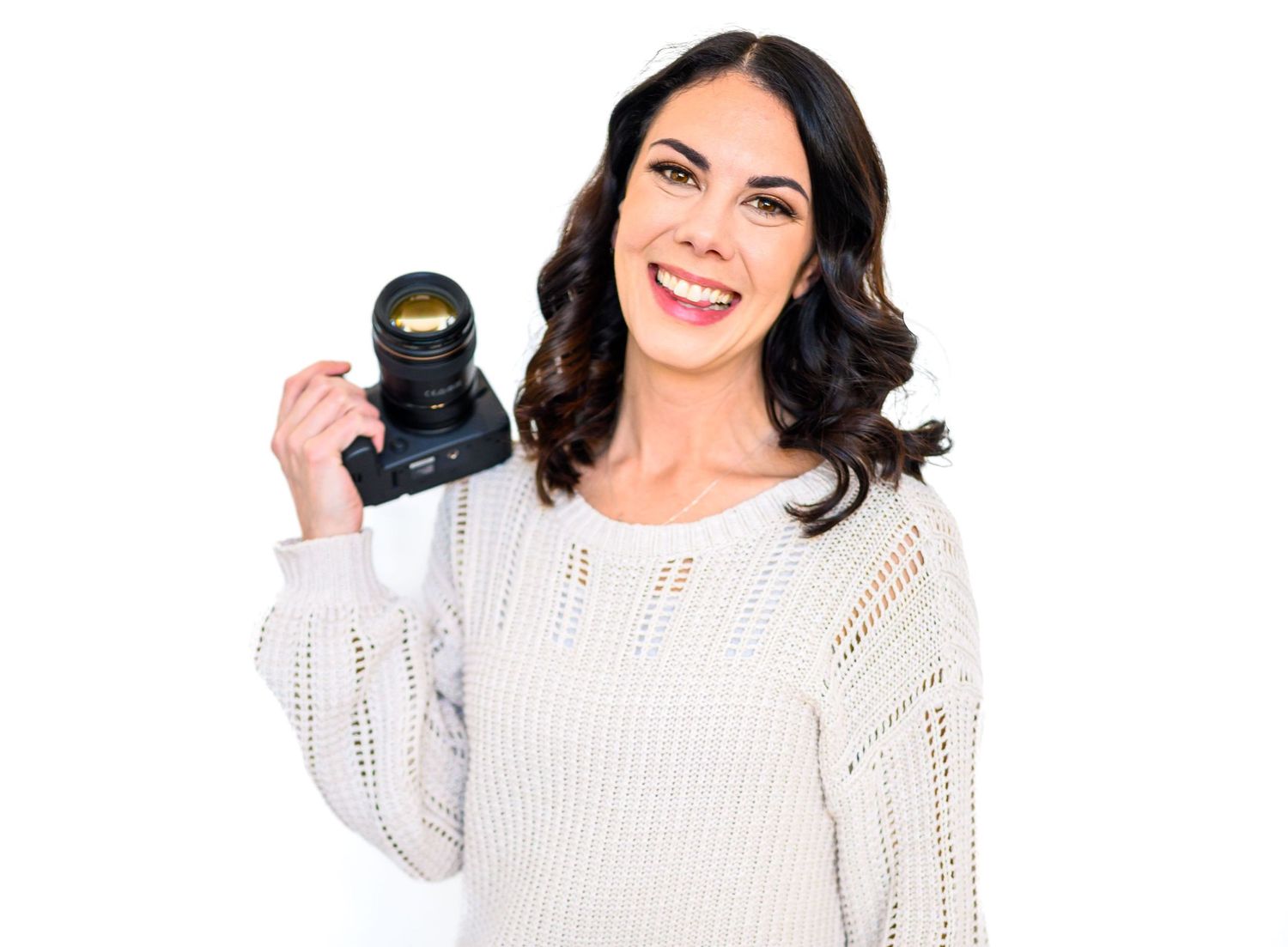 A Raleigh NC family photographer holds her camera at her shoulder and smiles against a white background.