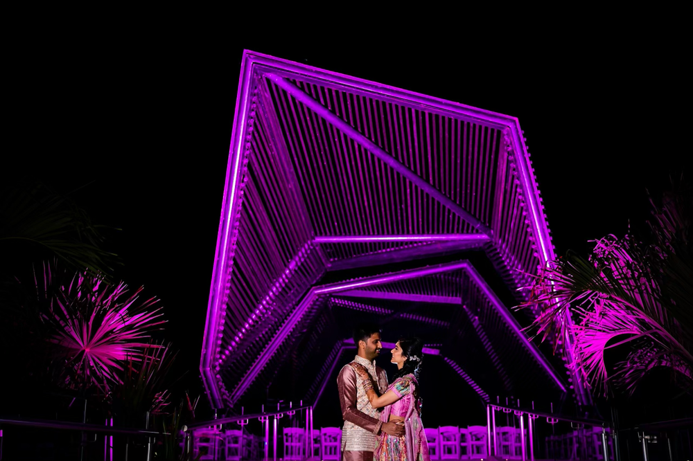 Illuminated geometric purple wedding arch structure glowing against dark night sky.