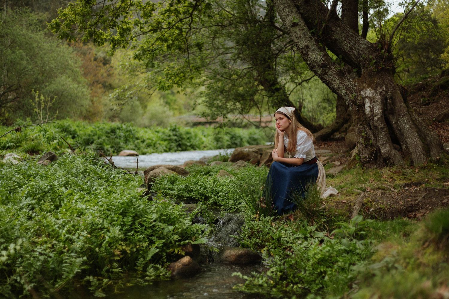 mulher aldeã de camisa saia avental lenço na cabeça junto a rio árvore floresta aldeia cottagecore fantasia