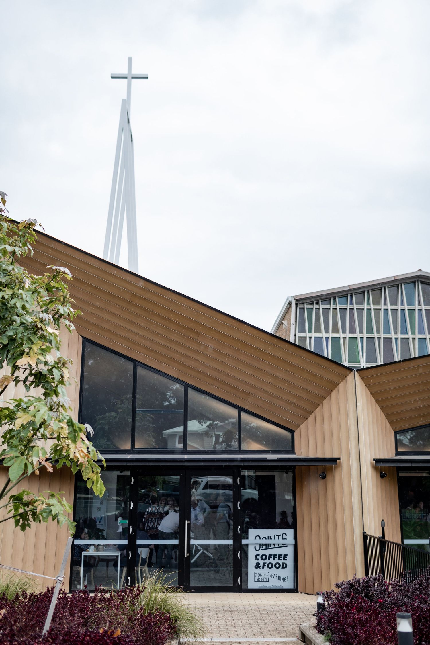Modern church exterior with angular architecture and prominent cross spire against cloudy sky.