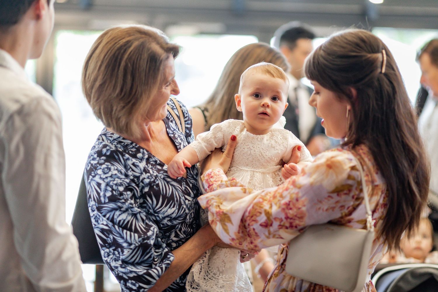 Gathering of people at a christening celebration with baby in white dress.