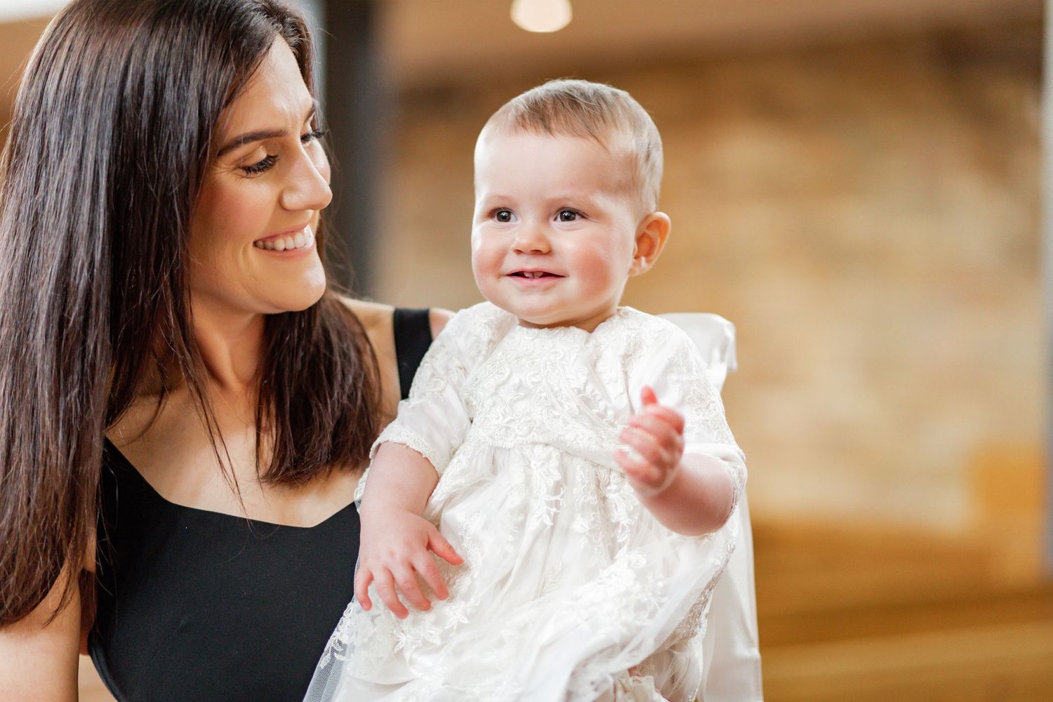 A baby dressed in white celebration attire is held while smiling at the camera.