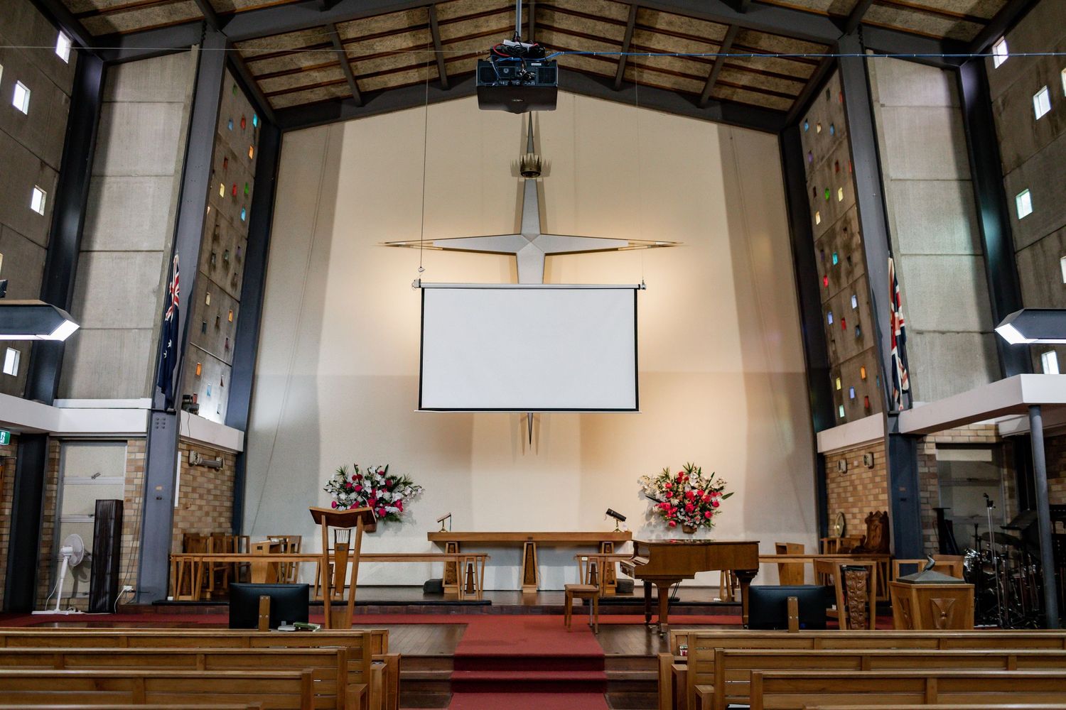 Modern church sanctuary interior with projection screen and wooden cross mounted on white wall.