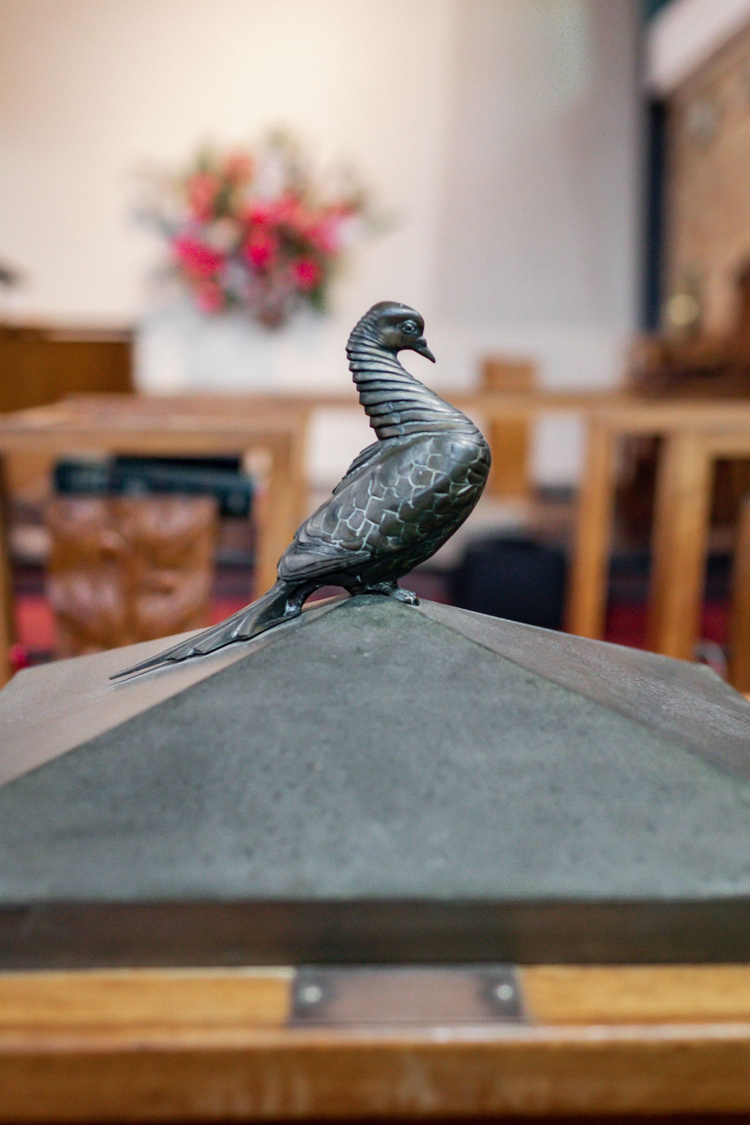 Decorative metal bird sculpture perched on wooden church furniture.