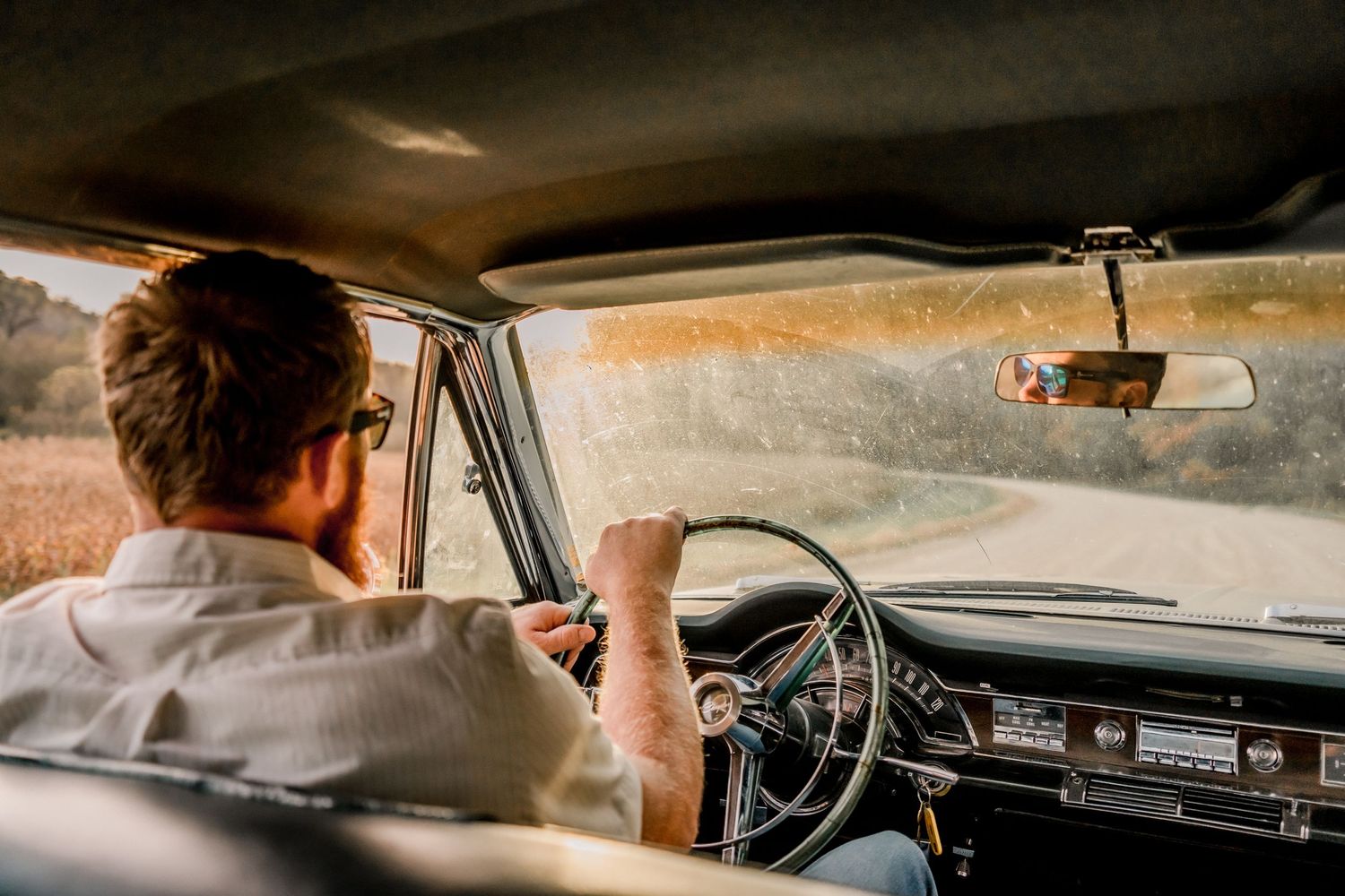 Person driving a vintage car with retro dashboard visible through windshield.
