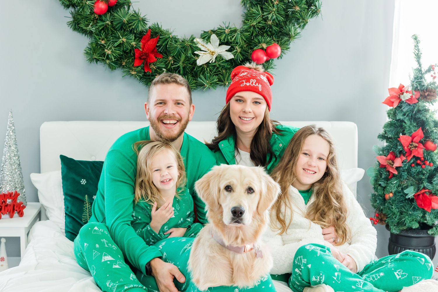 Holiday family photo with golden retriever in matching green pajamas by Christmas wreath.