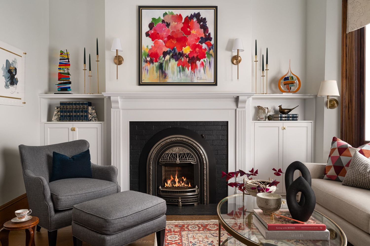 Cozy living room with fireplace, red floral artwork, and grey upholstered furniture.
