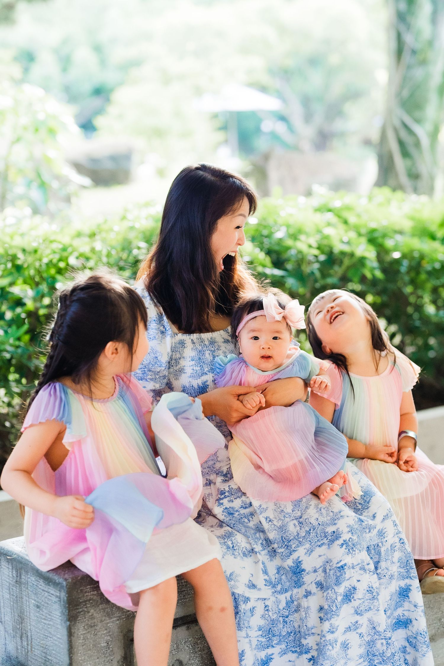 A family having a joyful moment outdoors with children in pink dresses surrounded by greenery.