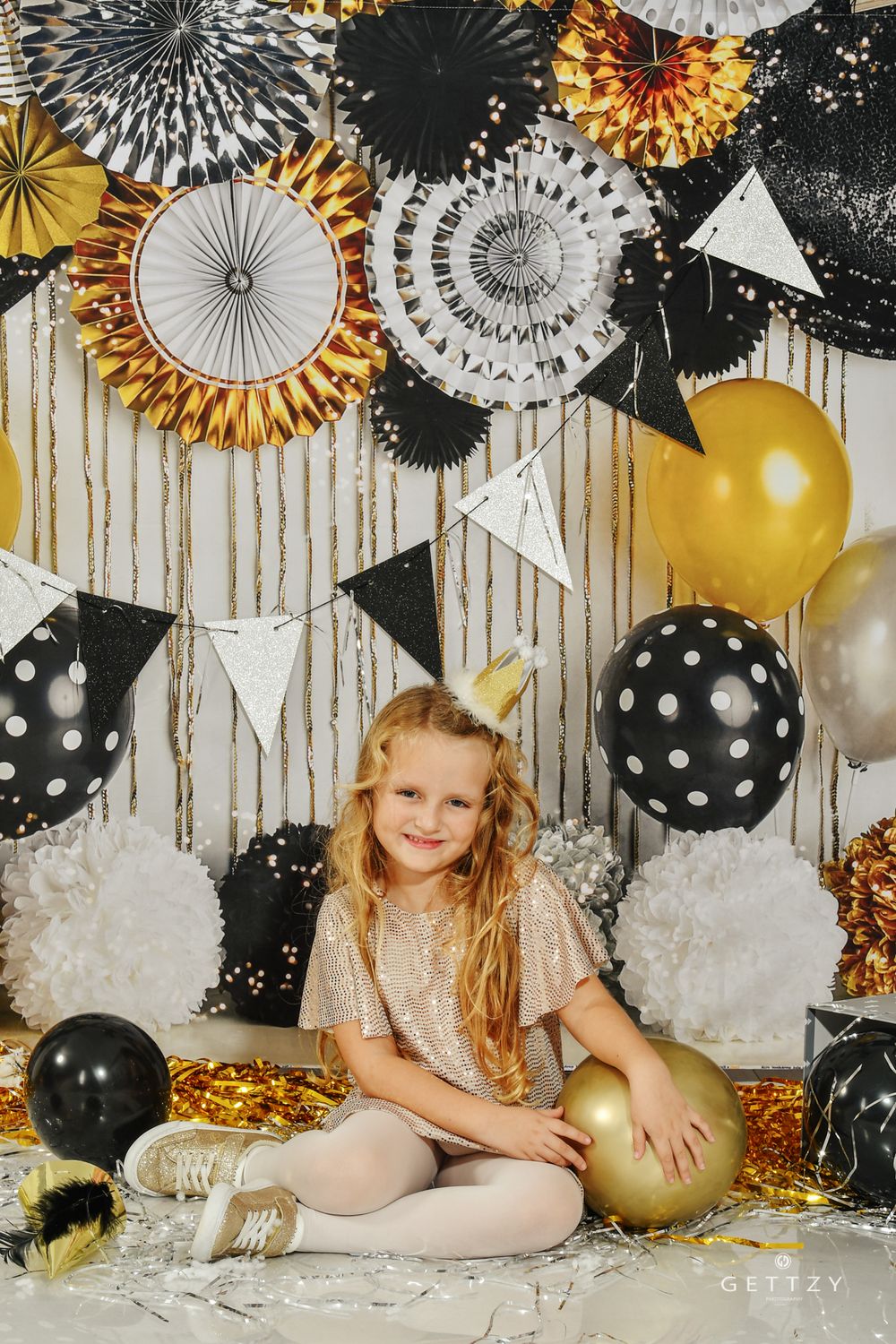 Birthday backdrop with gold and black paper fans, polka dot balloons, and white bunting.