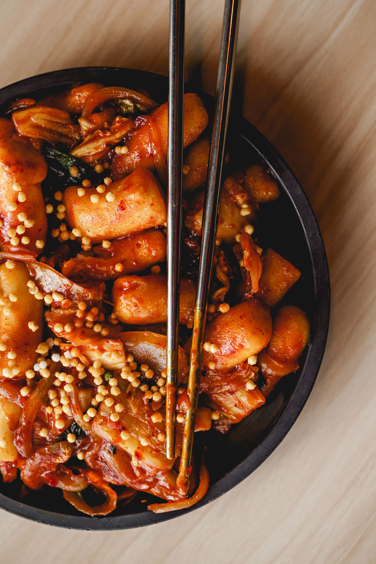 Spicy Korean chicken dish topped with sesame seeds served in black bowl with chopsticks.
