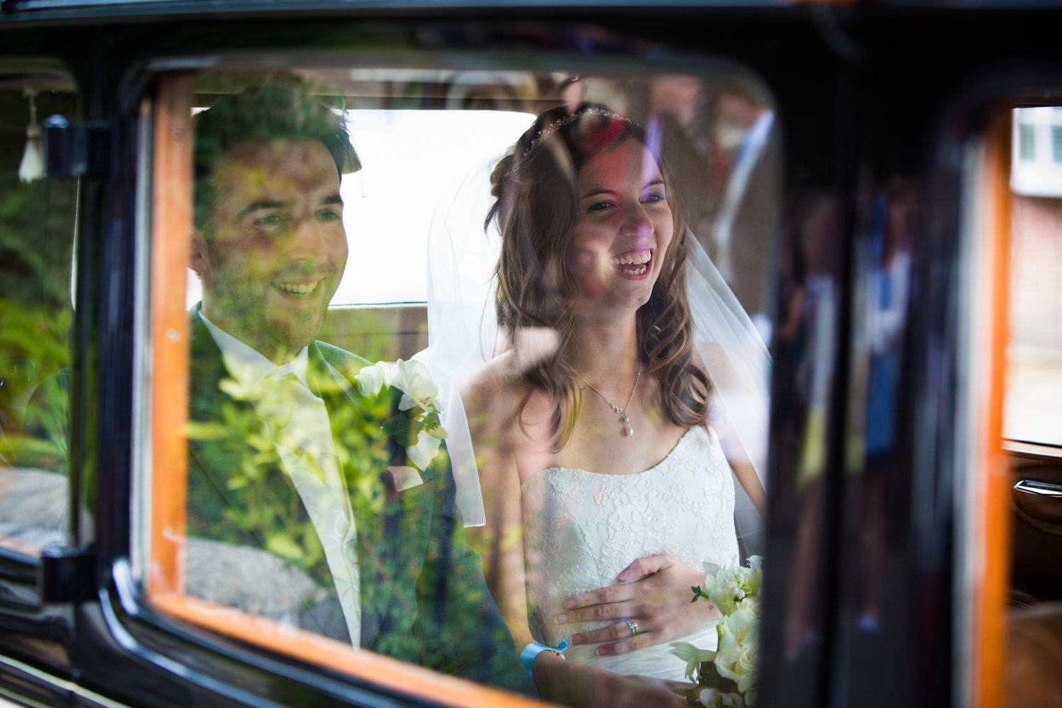 Wedding couple seen through vintage car windows with reflective effects.