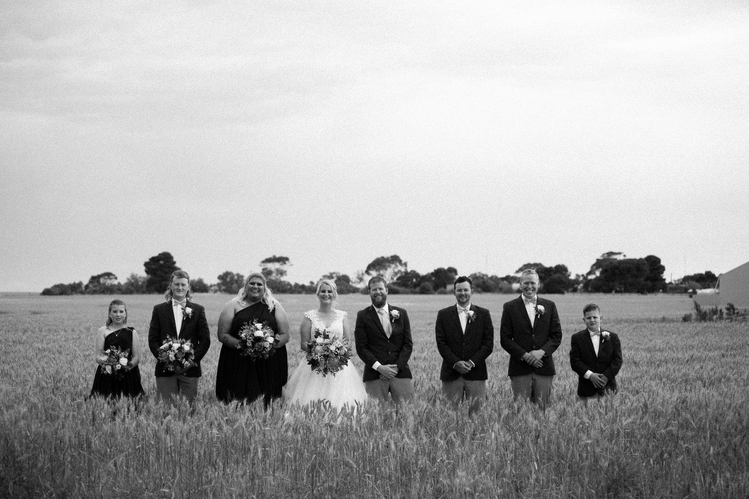 large bridal party in black and white with grass coming up past their knees.