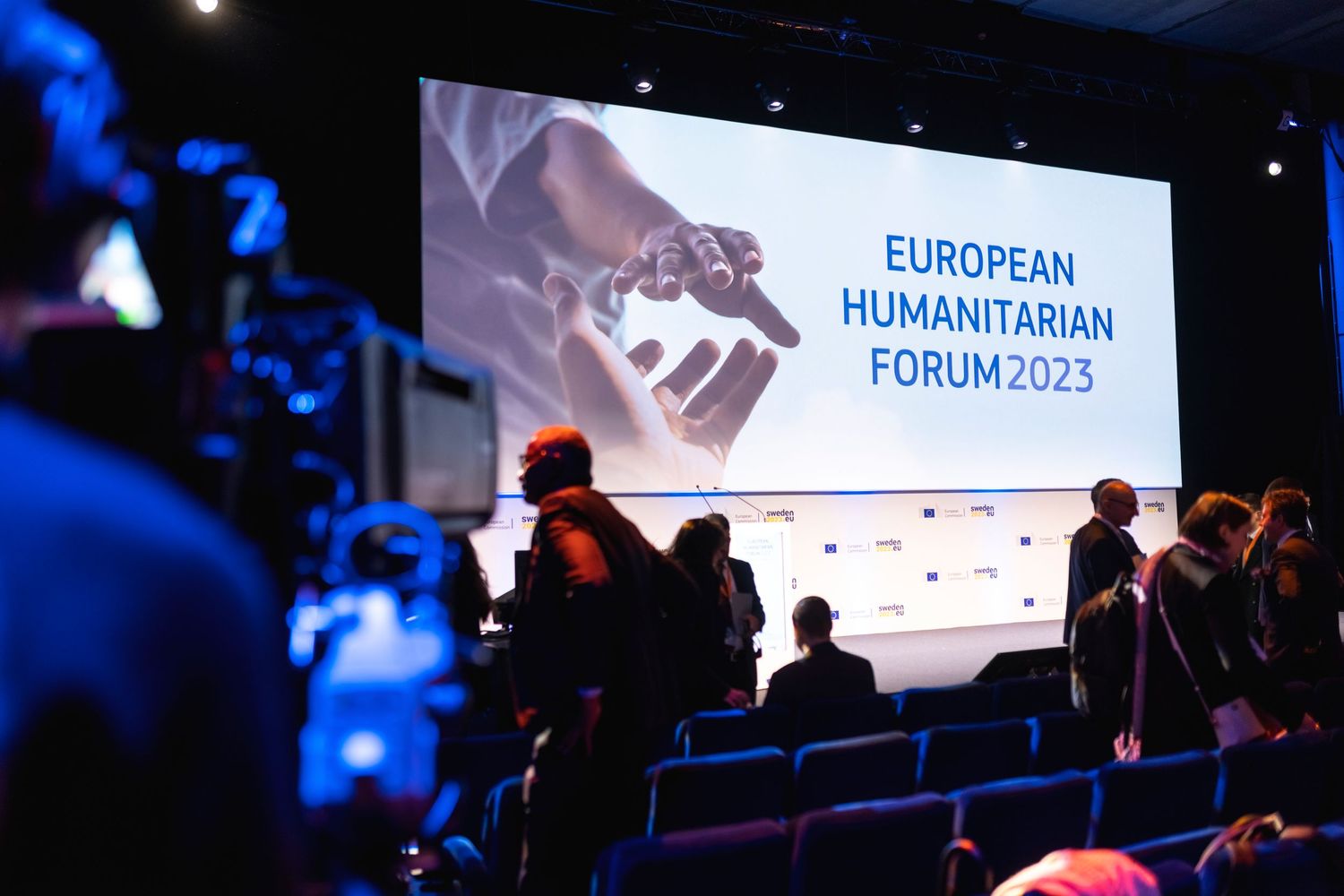 European Humanitarian Forum 2023 conference stage setup with audience silhouettes and blue lighting.