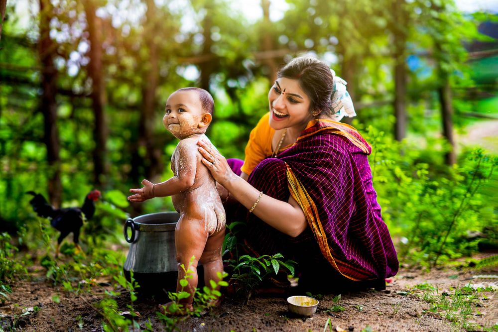 Artistic shot of a mom getting her one year baby boy bathed in a village shot by creative kids photographer