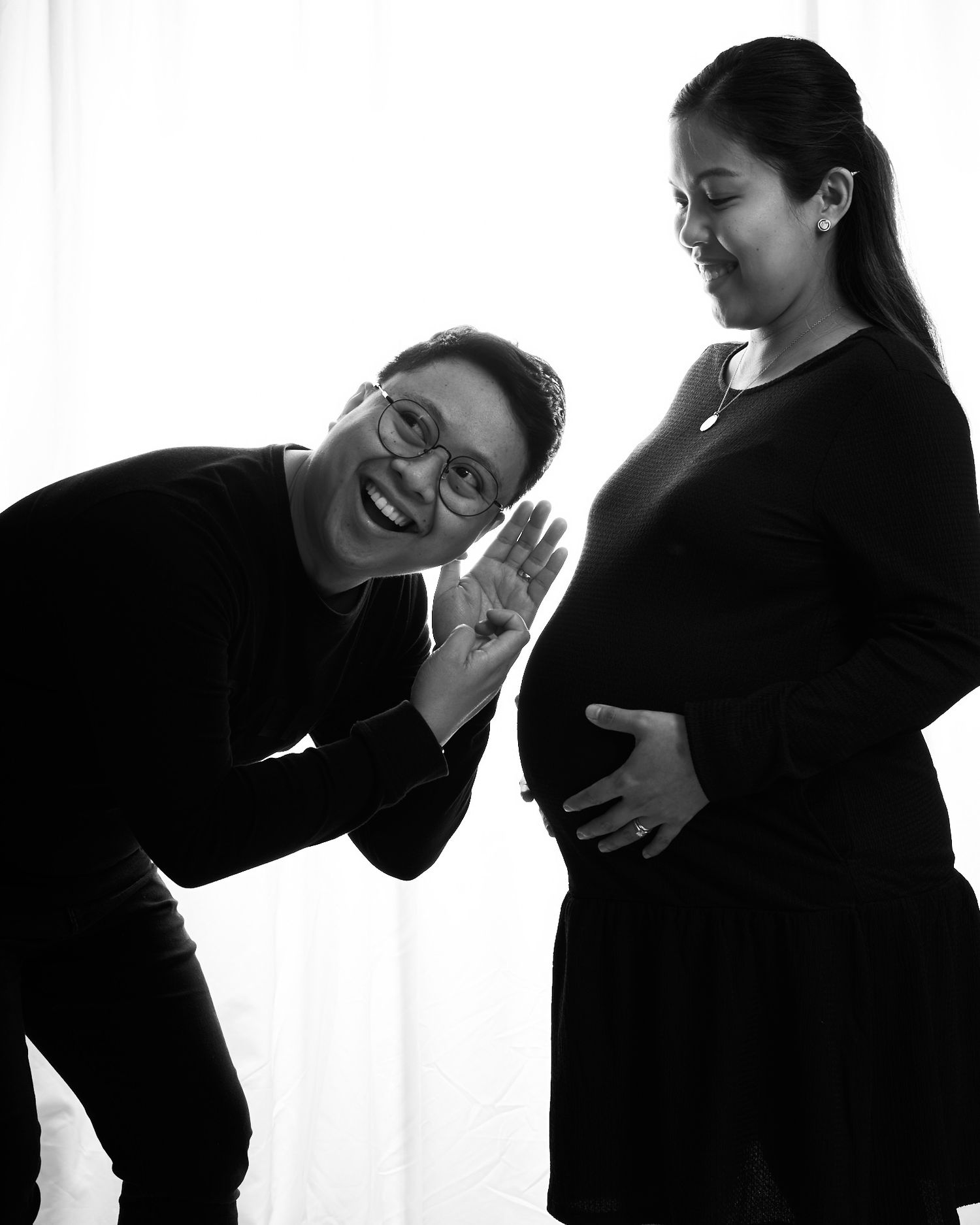 Black and white silhouettes capture playful interaction between two people against bright window.