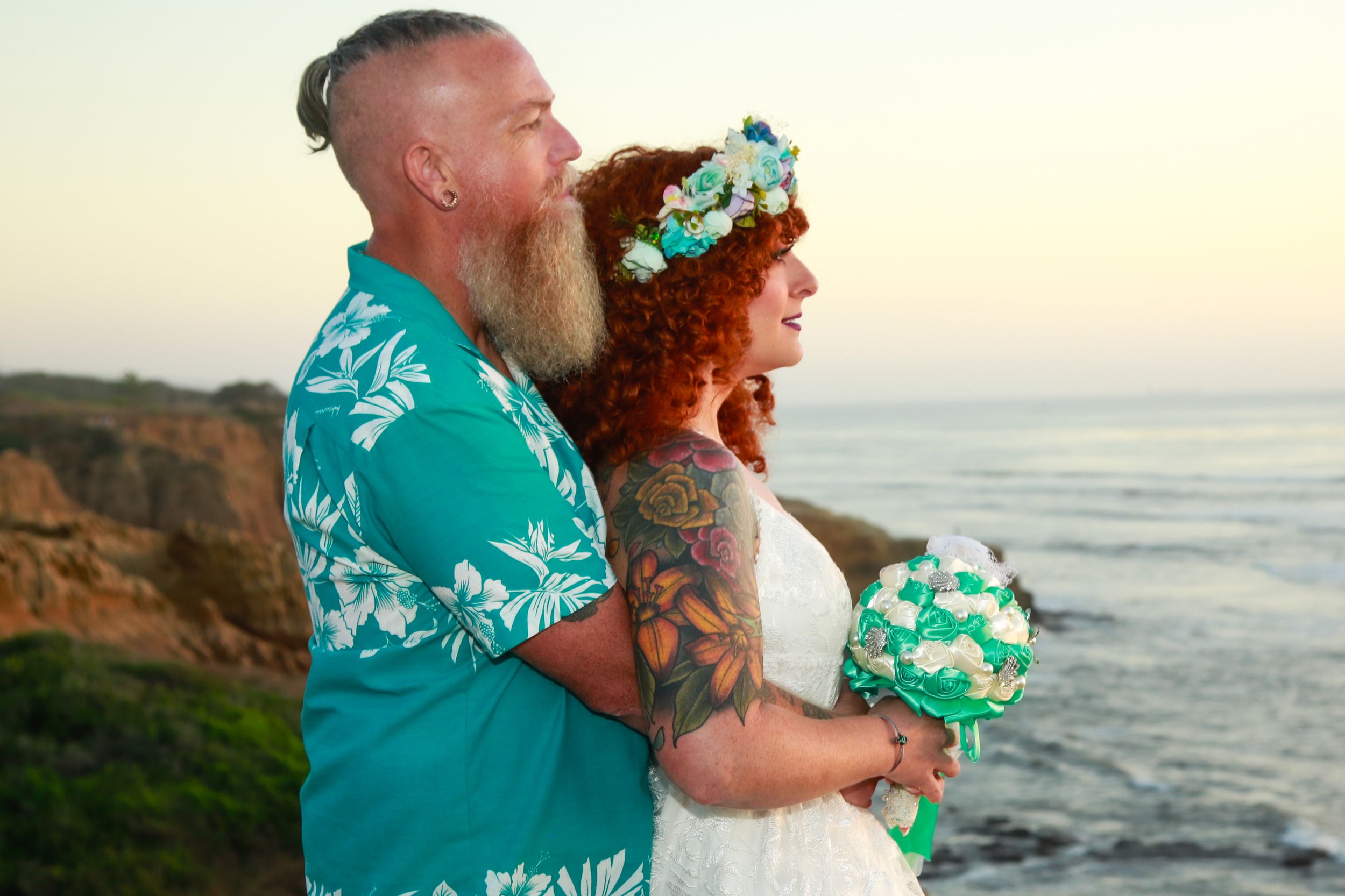 A couple embraces on a scenic coastal cliff during their beach wedding.