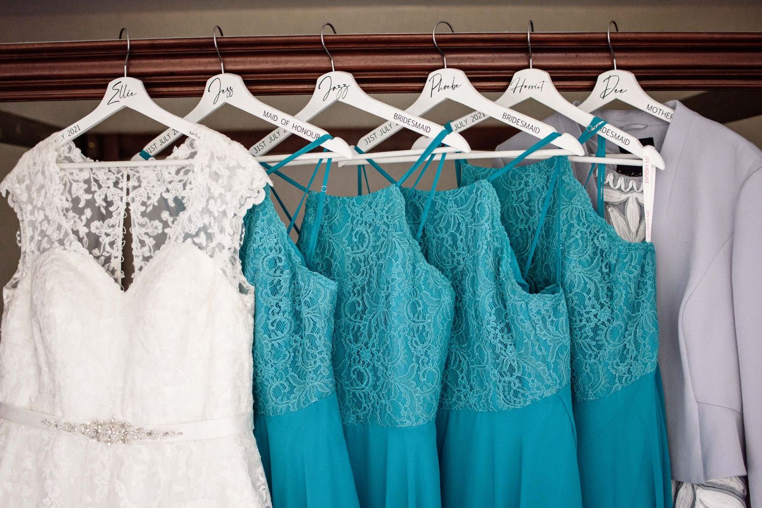 Wedding dresses in white and turquoise hanging on white hangers displaying lace details.