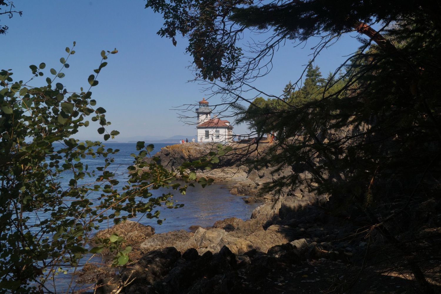 Coastal lighthouse stands on rocky shoreline overlooking blue ocean waters.