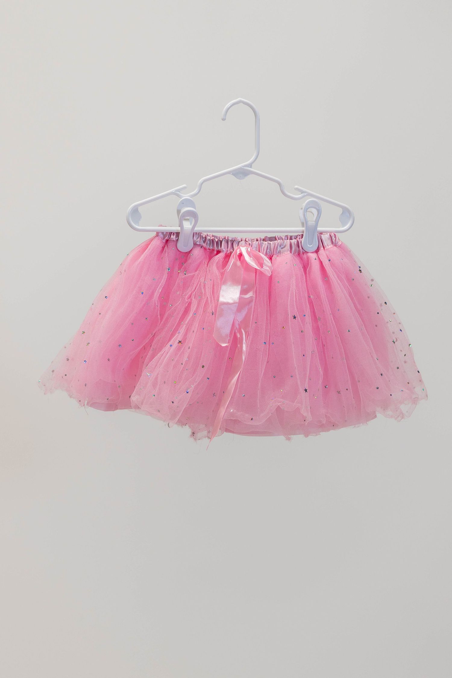 Pink sparkly tutu skirt with glitter details hanging on white plastic hanger.