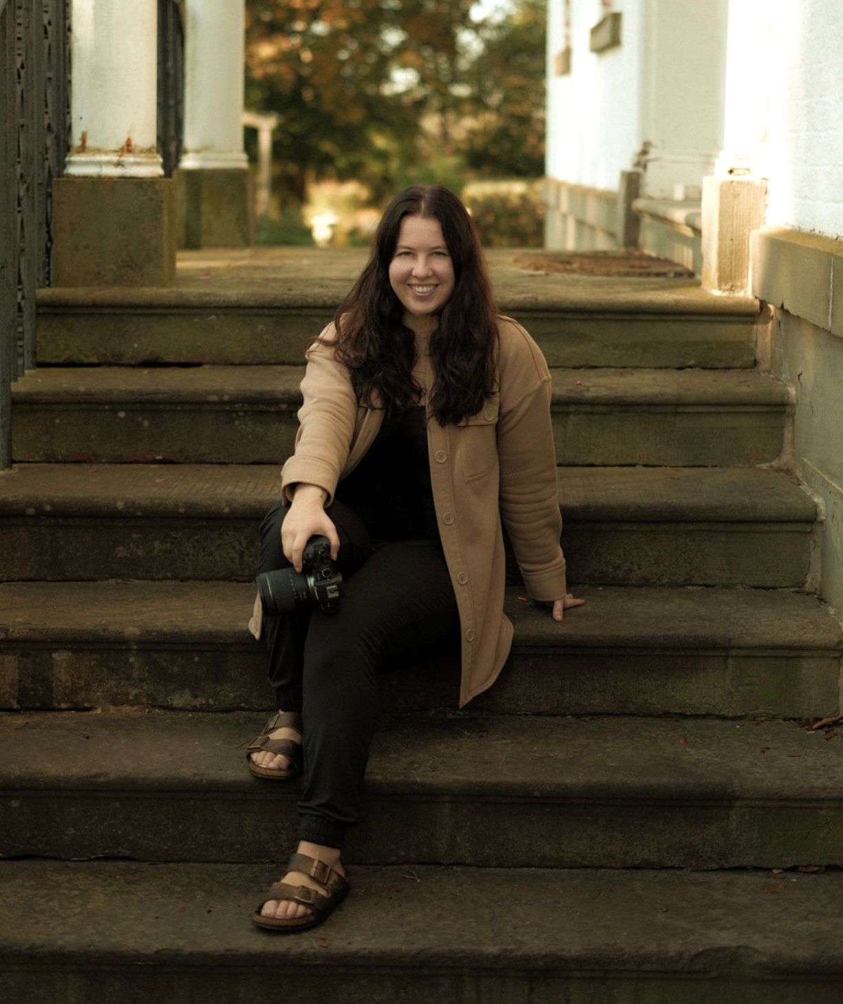 Person in brown jacket sitting casually on outdoor steps.