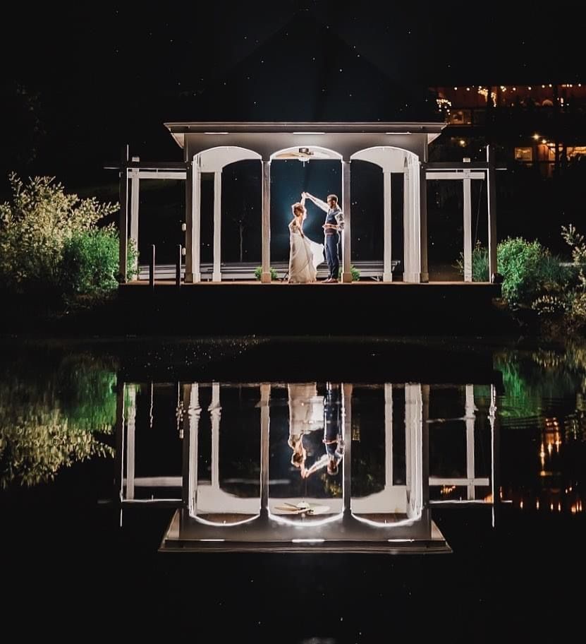 Nighttime wedding portrait in a white gazebo reflecting perfectly in still water.