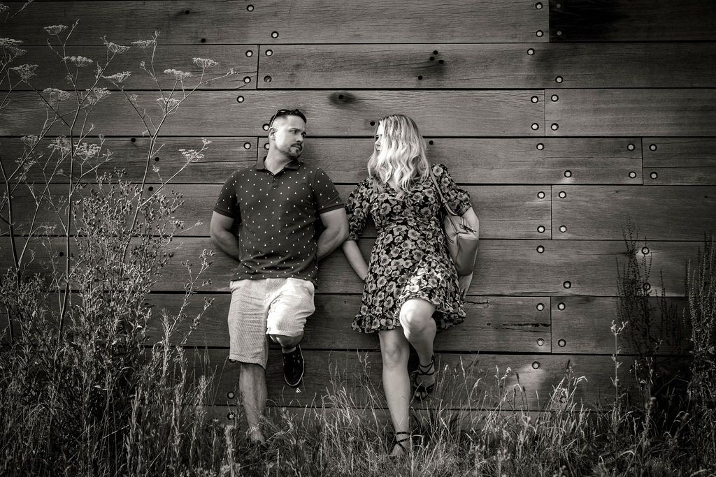 A black and white portrait of a couple sitting against a wooden wall.
