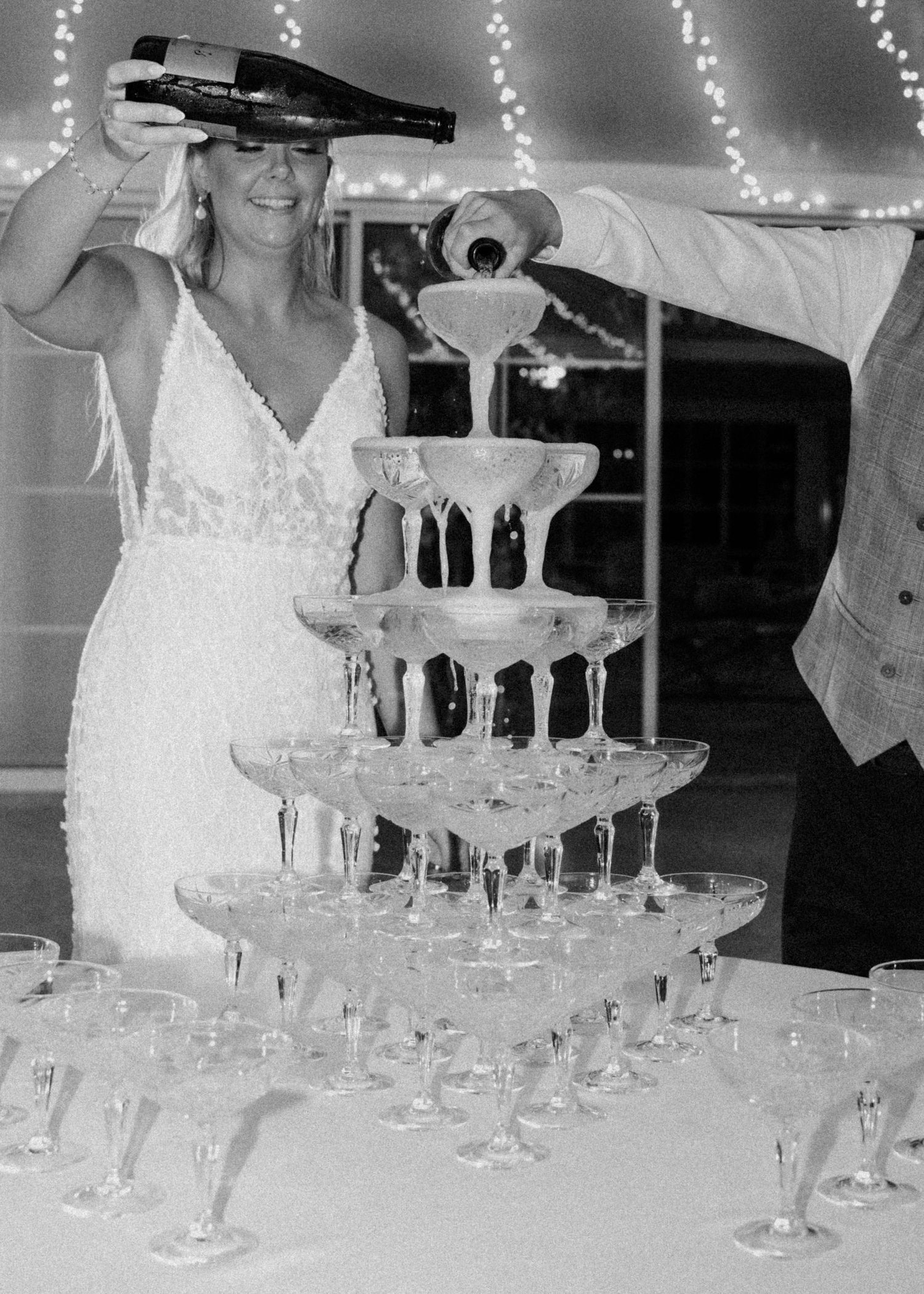 Black and white photo of a champagne tower being filled at an elegant wedding reception.