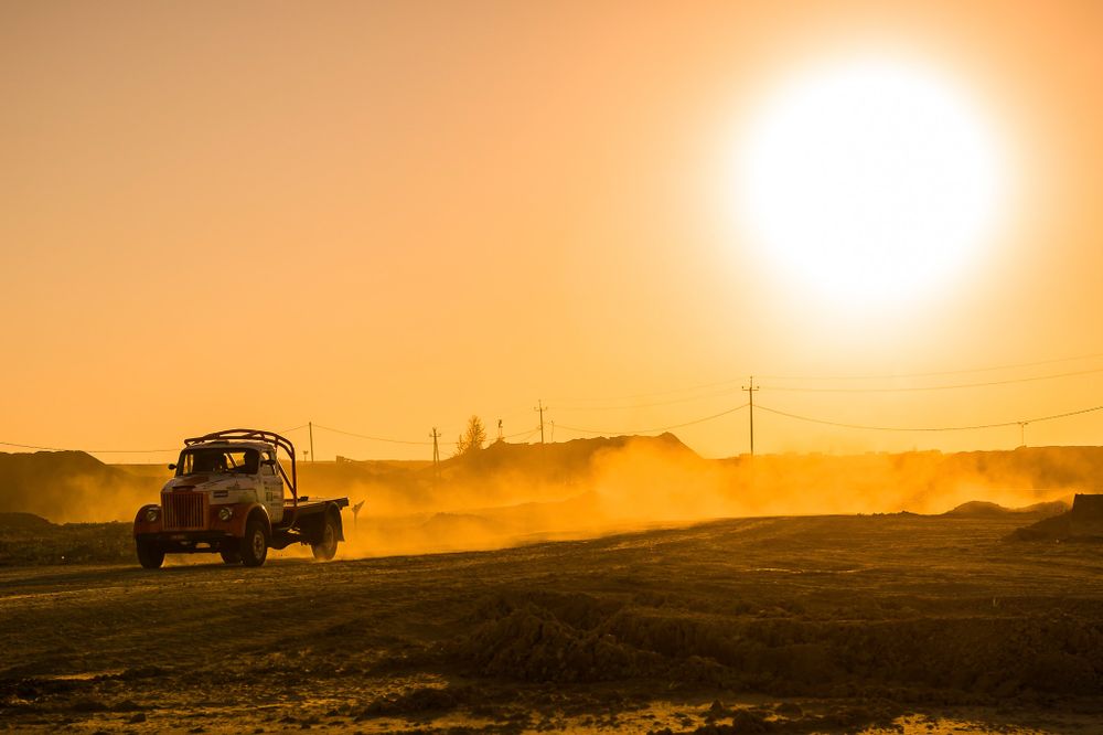Off-road vehicle silhouetted against golden sunset with dust trails.