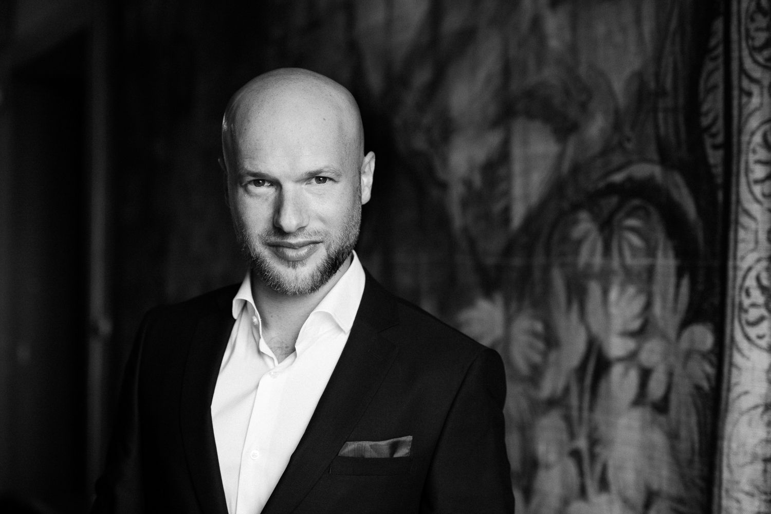 A dramatic black and white portrait of a man in formal attire against a textured background.