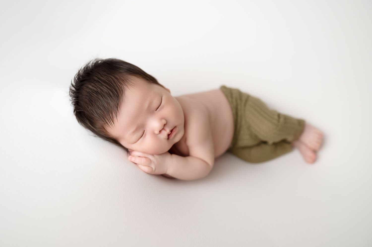 Peaceful sleeping newborn in olive shorts on white background.