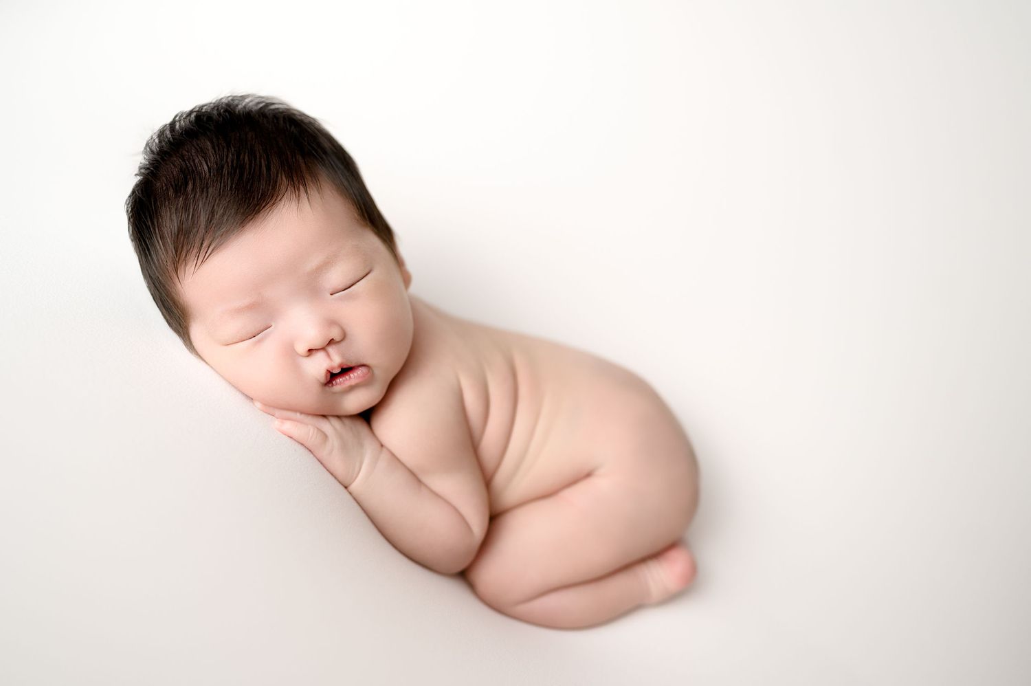 Sleeping newborn in fetal position on white background.