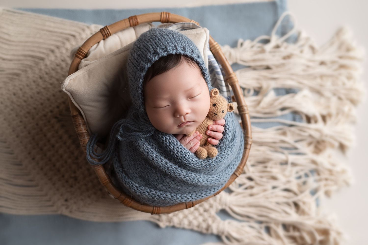 Peaceful newborn in gray knitted wrap sleeping in round wooden bowl.