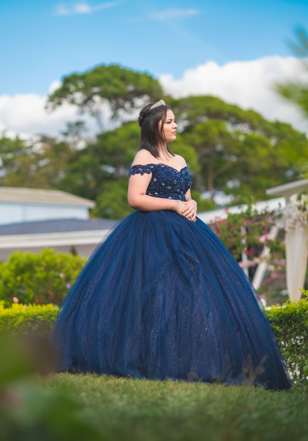 Off-shoulder navy ballgown showcased in an elegant outdoor portrait against greenery.