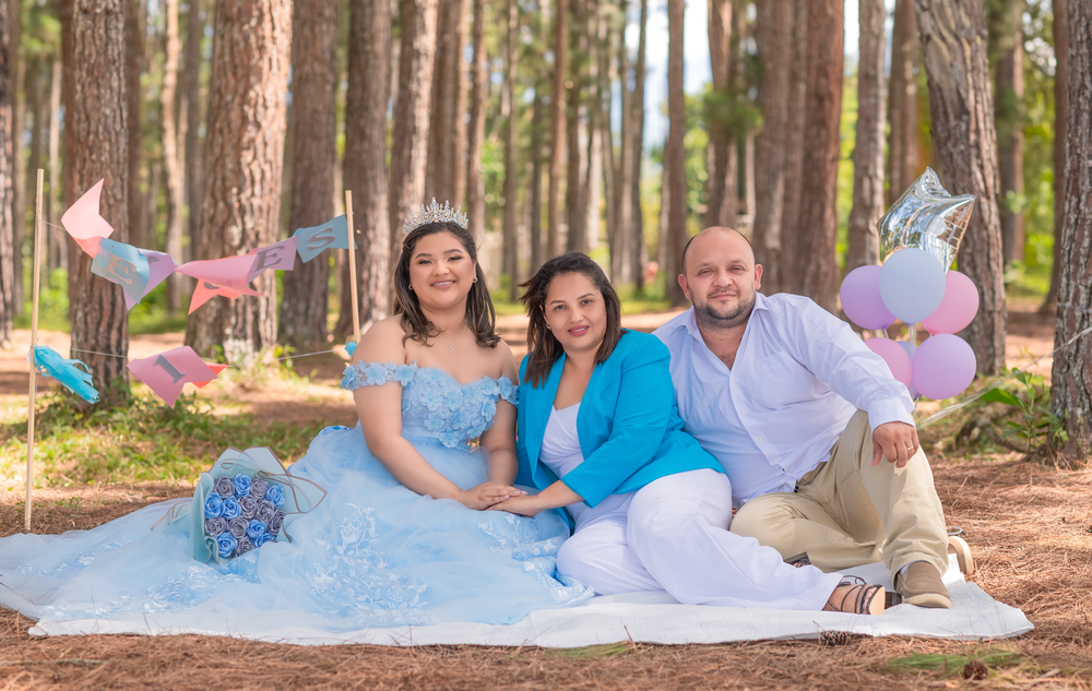 Family photo session in a pine forest with light blue gown and casual attire.