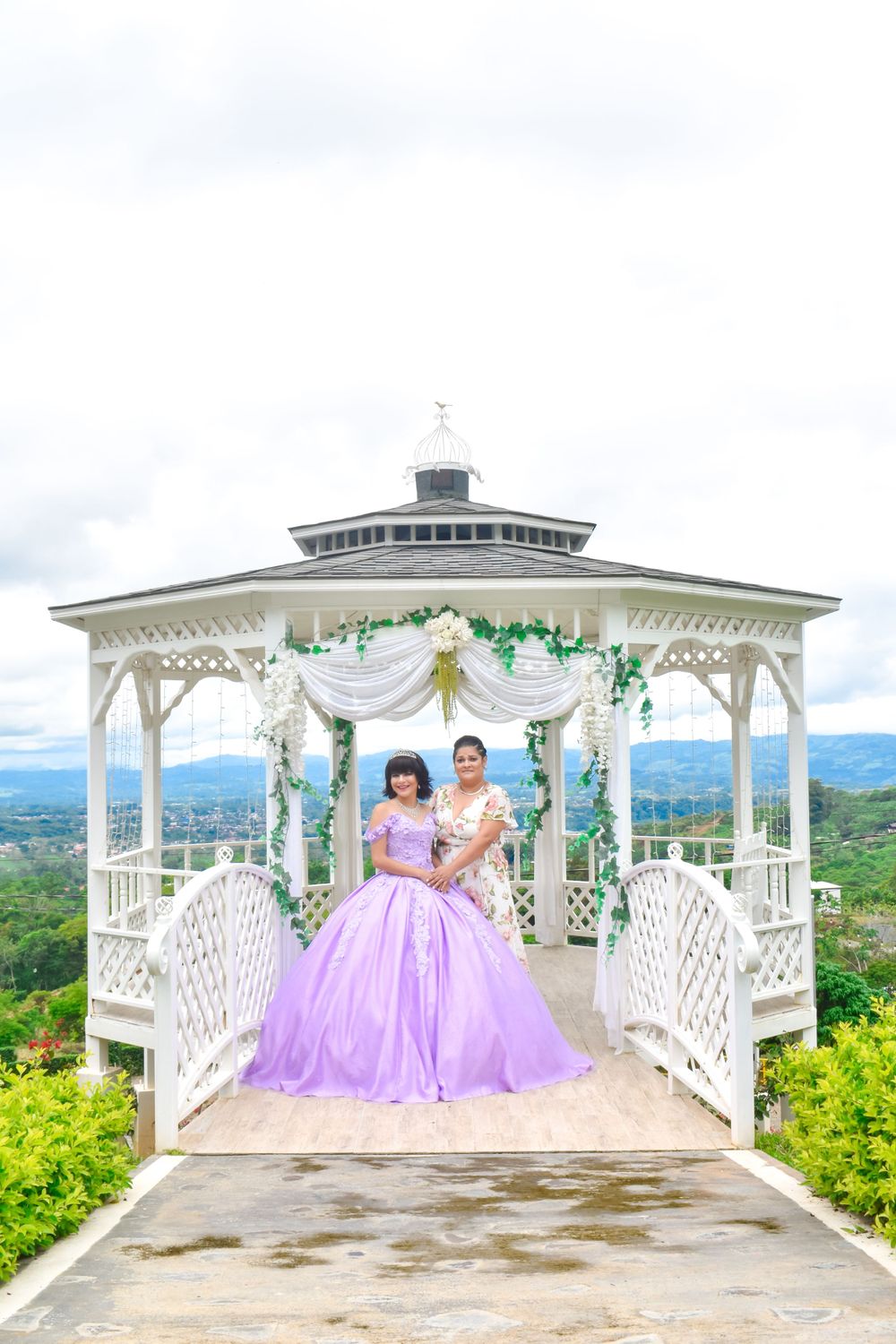 Lavender ball gowns in a decorated white gazebo overlooking a mountain landscape.