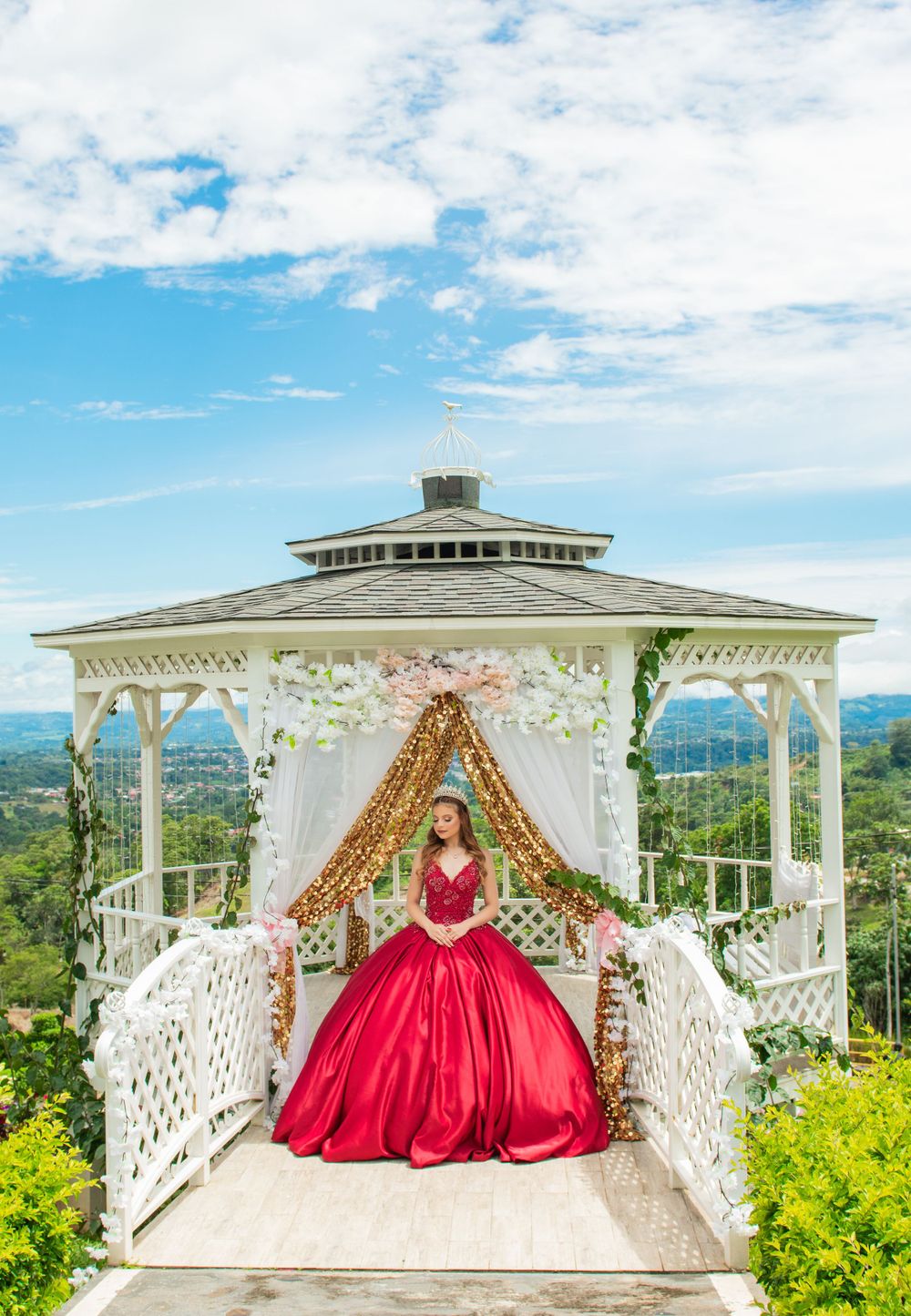 Majestic red ballgown captured in a white gazebo overlooking mountain scenery.