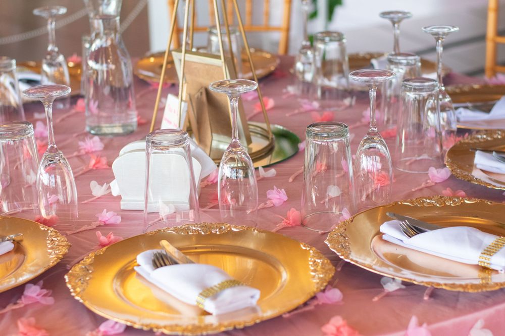 Elegant table setting with gold charger plates, wine glasses and pink tablecloth for a formal dining event.
