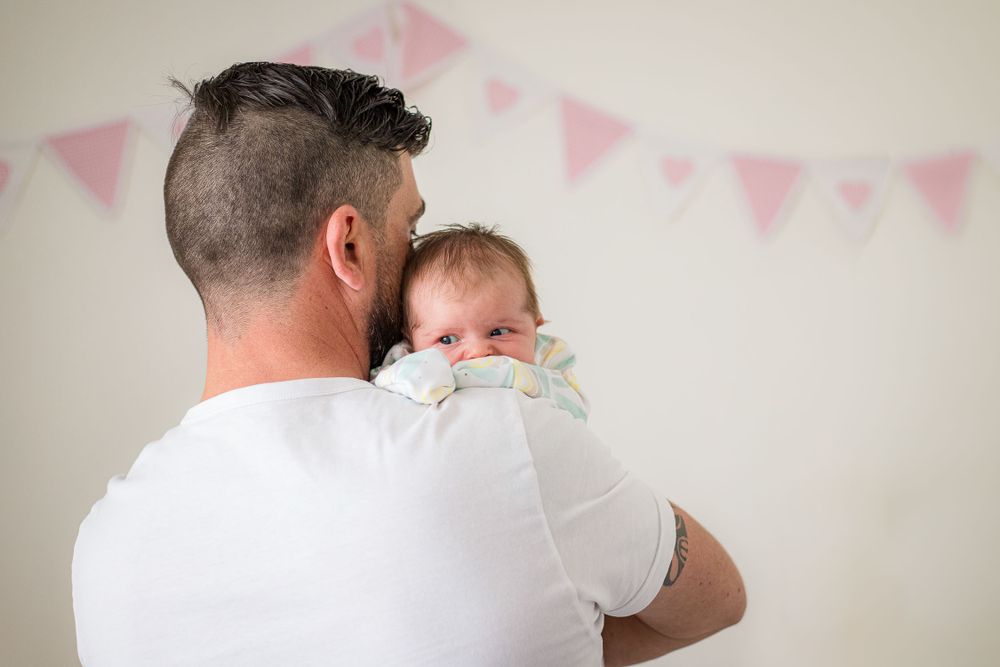 dad holding baby on his shoulder and baby looking over dad's shoulder in bedroom