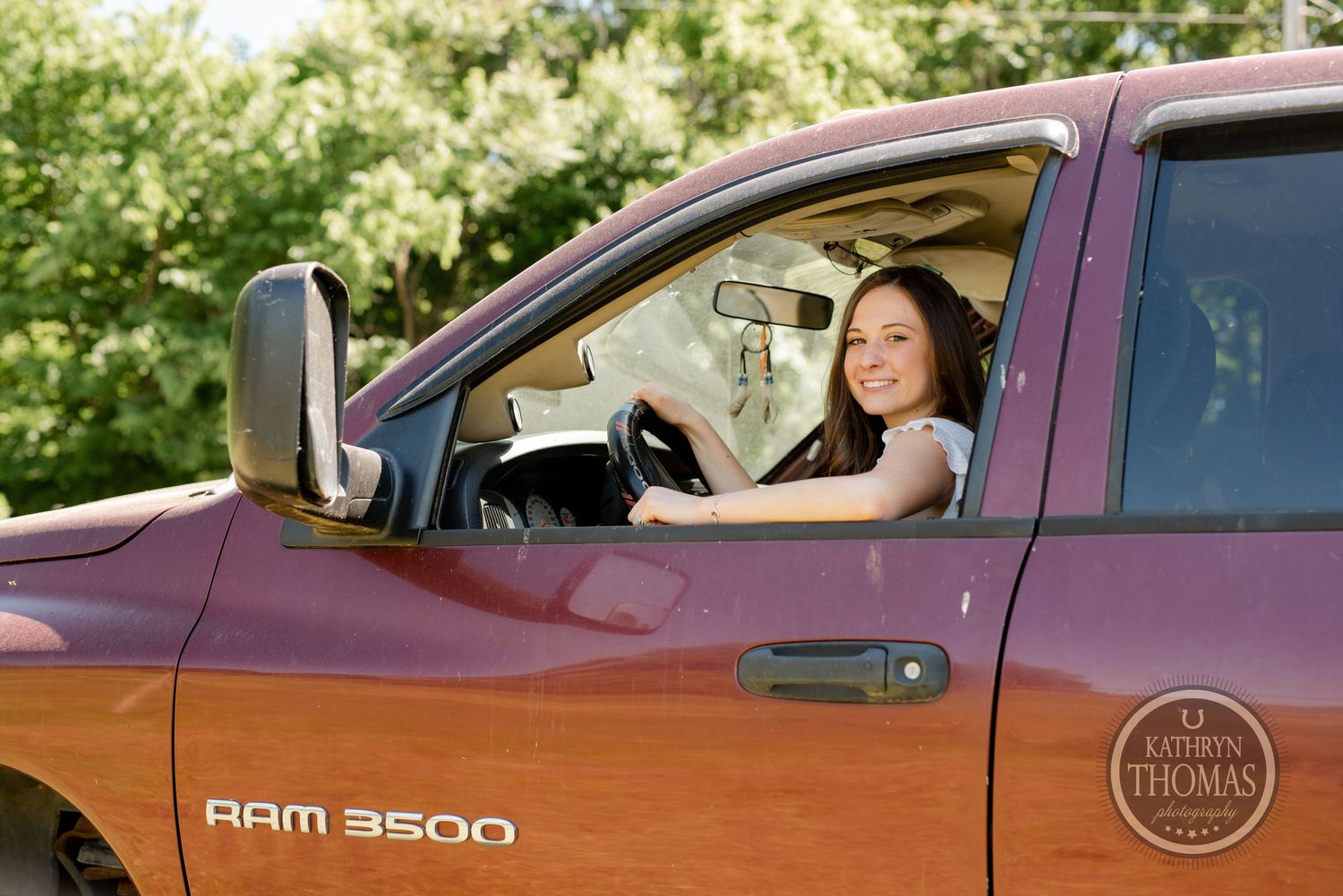 Driver poses in red Ram 3500 pickup truck against green foliage background.